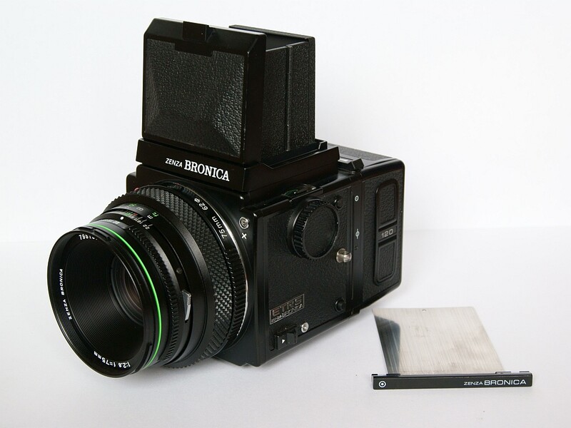 Bronica SQ film camera with lens, prism finder, and instruction manual on white background.