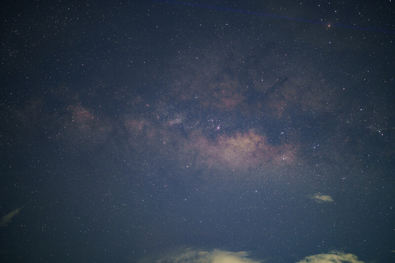 Milky Way galaxy stretching across a starry night sky above clouds on the horizon.