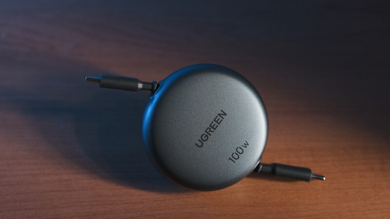 Ugreen Icrow portable device with retractable cables on wooden surface with warm studio lighting.