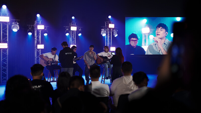 Panel of speakers seated on stage during an evening event with blue overhead lighting and a video screen displaying a speaker.