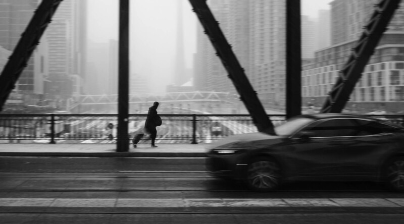 Person jogging on a bridge with blurred car and misty cityscape behind.