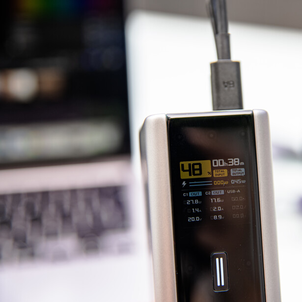 Portable power meter with digital display showing battery percentage and charge information, connected via USB cable.