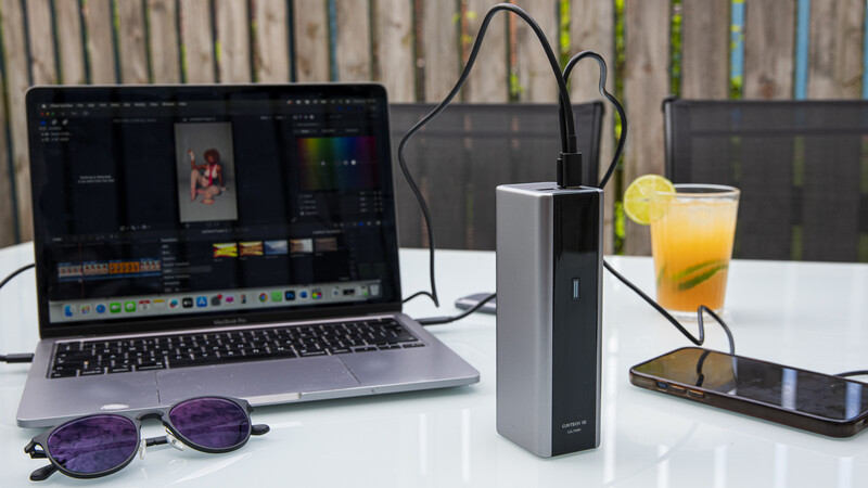 Creative workspace with laptop running video editing software, external storage device, smartphone, and beverage on white desk.