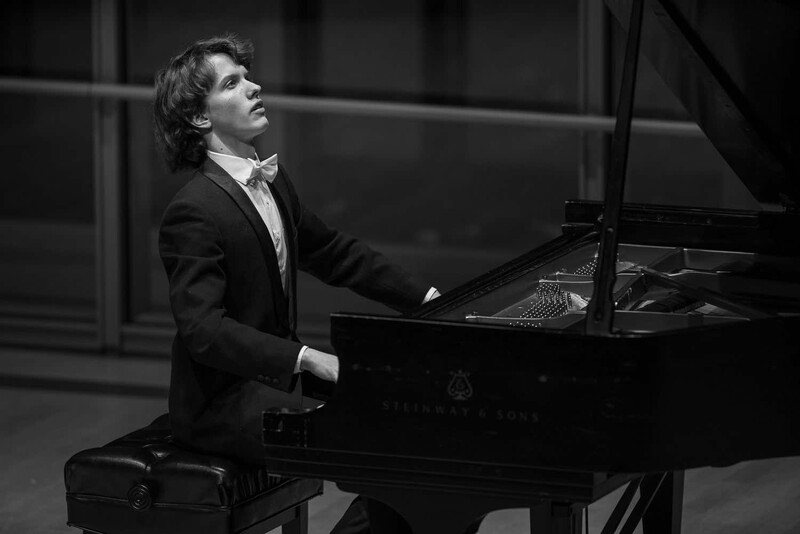 Pianist in formal attire seated at grand piano, gazing upward during performance in black and white.