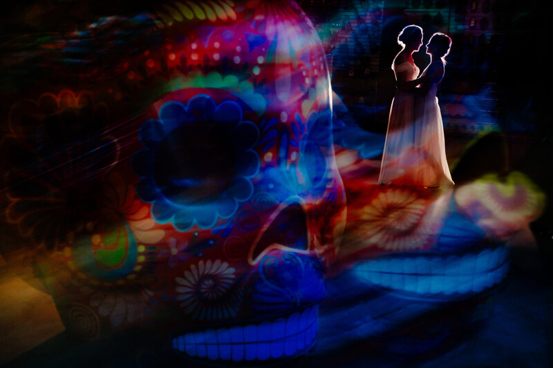 Silhouetted couple figure standing amid vibrant, colorful light projections and abstract patterns.