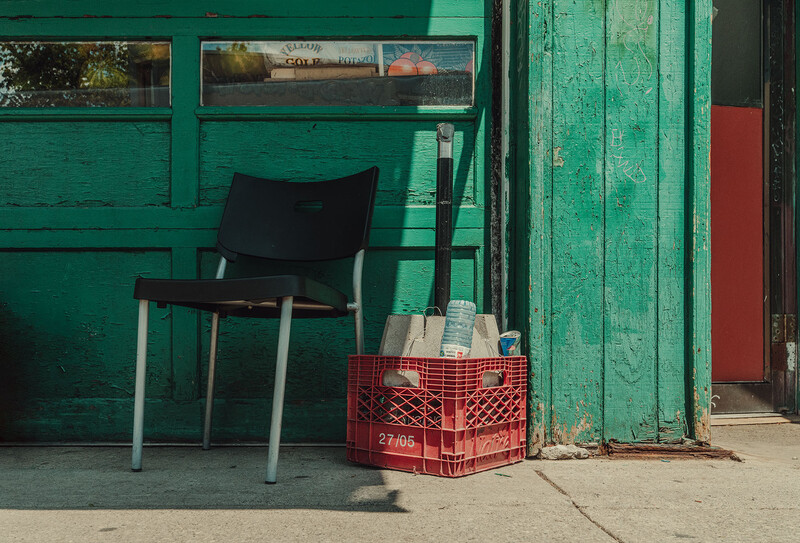 Black chair with metal legs against weathered green wooden wall next to red plastic crate.