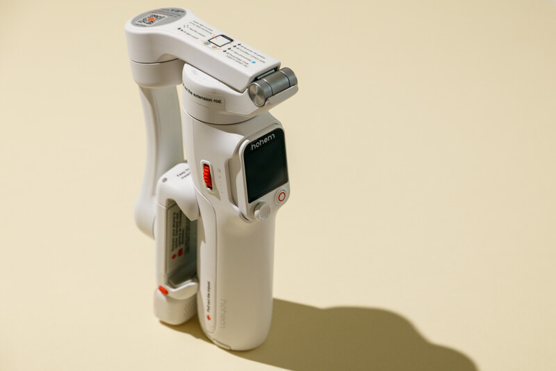 White compact digital camcorder with articulating screen and extendable lens, photographed against beige background.