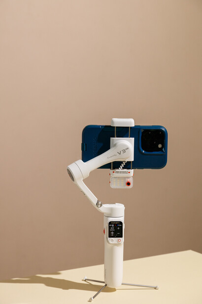 White smartphone gimbal stabilizer holding a phone against a beige background.