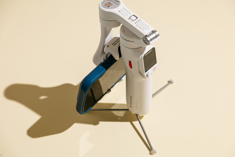 White and blue dental or medical imaging device mounted on articulating arm casting shadow on beige background.