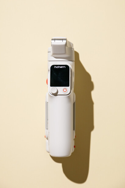 White handheld thermal imaging camera with small display screen against beige background.