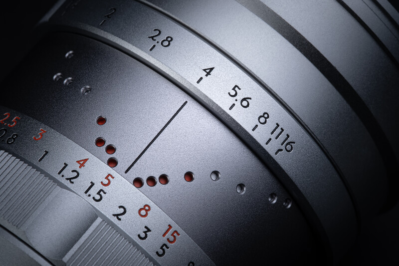 Close-up of camera lens barrel showing aperture markings and depth-of-field scale with red reference dots.