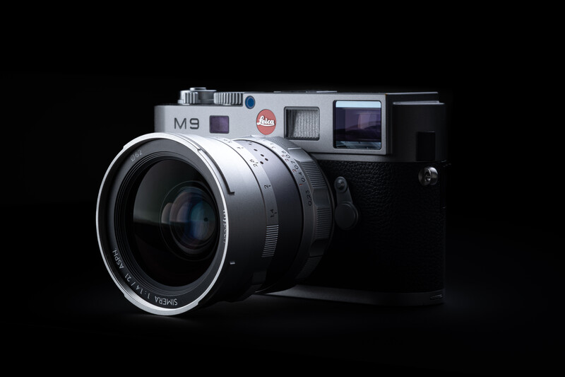 Leica M9 rangefinder camera with silver top plate and black body, shown with attached lens against black background.