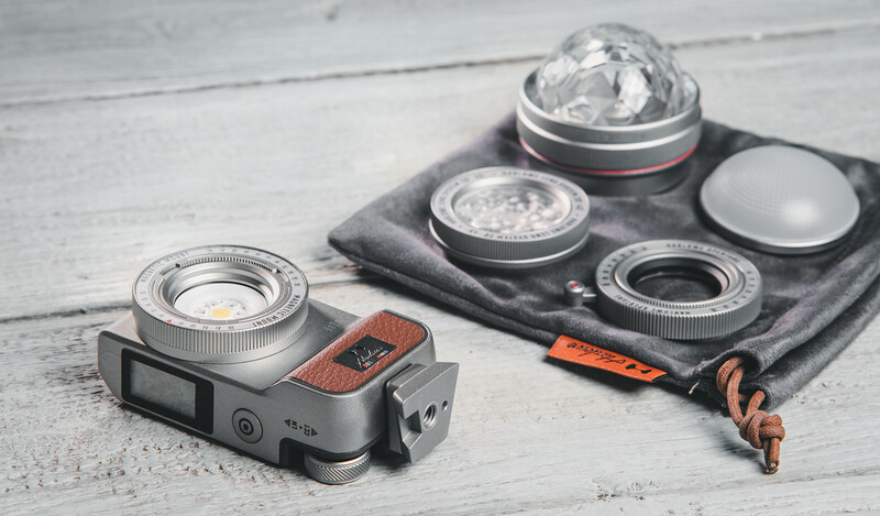 Vintage rangefinder camera with 35mm lens alongside three additional lenses and accessories on a gray cloth.