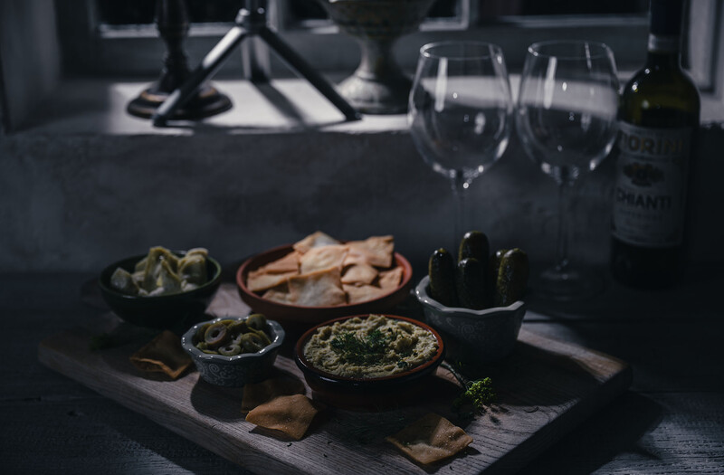 Overhead flat lay of appetizers and wine on a dark slate board with wine glasses and bottle in background.