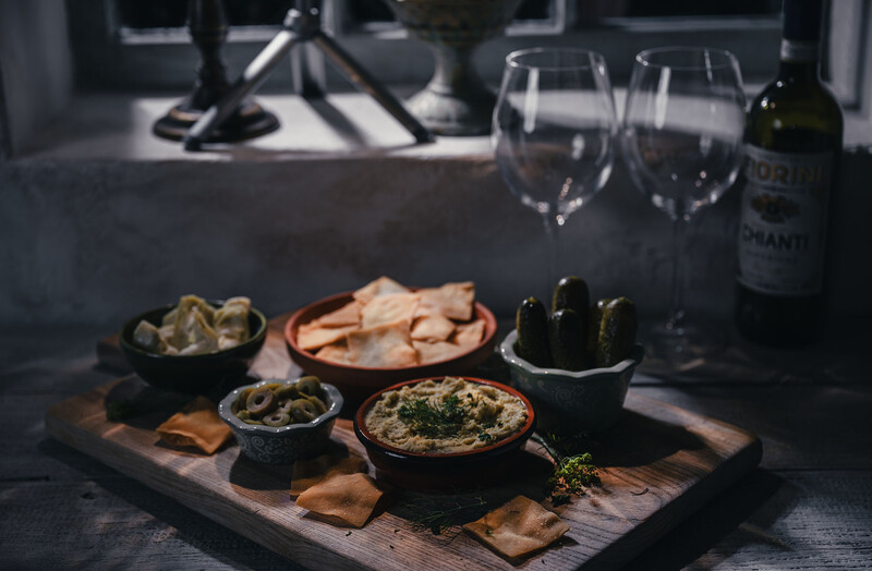 Food and wine styled flat lay with appetizers, dips, and wine glasses on a wooden board.