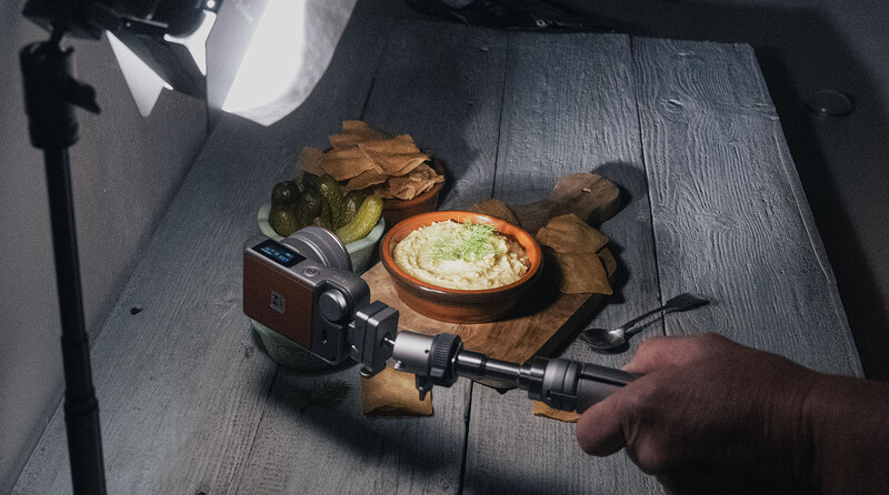 Food photography setup with video camera filming styled flatlay of appetizers and dip on wooden cutting boards.