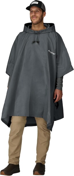 Model wearing a dark gray rain poncho over khaki pants and hiking boots, styled with a dark cap.