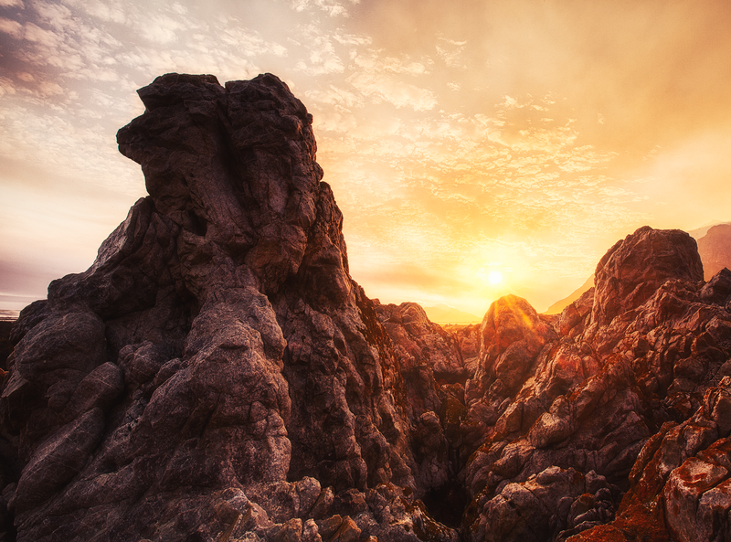 Dramatic rocky peaks silhouetted against a golden sunset sky with warm orange and purple tones.