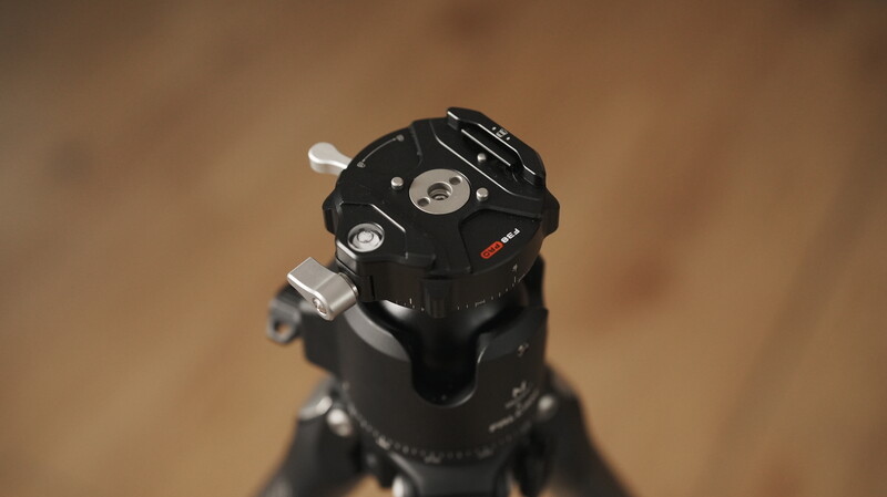 Close-up of a fluid head tripod with pan and tilt adjustment knobs, mounted on a blurred wooden background.