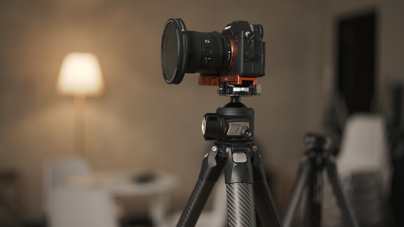 Mirrorless camera with wide-angle lens mounted on carbon fiber tripod in studio setting.