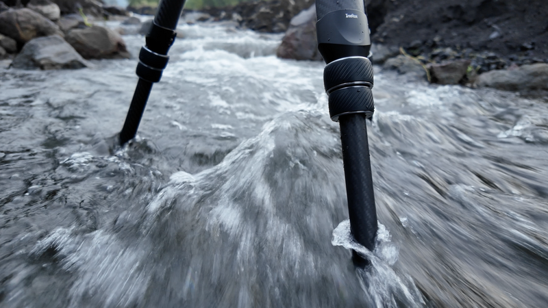Two trekking poles planted in fast-flowing water during river crossing.