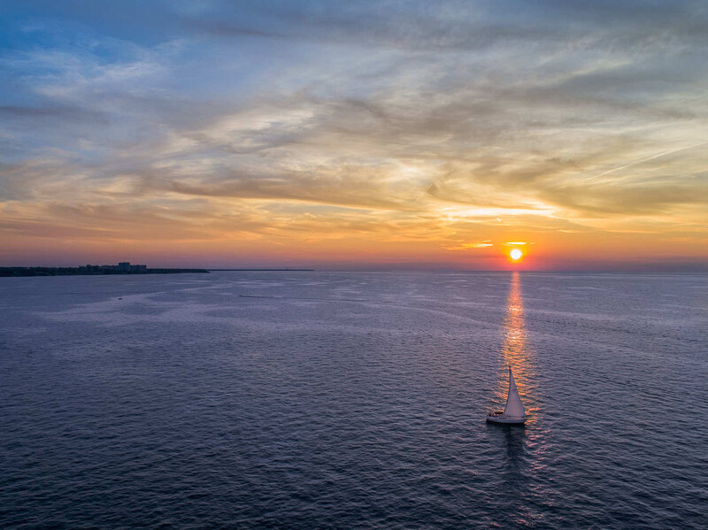Sailboat silhouetted against golden sunset over calm ocean waters.