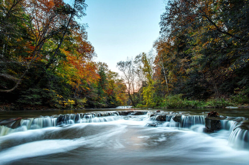 Cascading waterfall flowing through a forested river landscape during autumn.