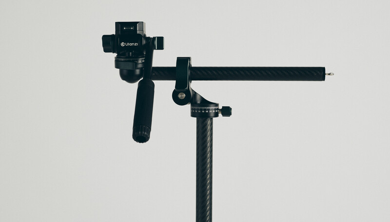 Gimbal stabilizer with pan-tilt head mounted on carbon fiber pole against white background.