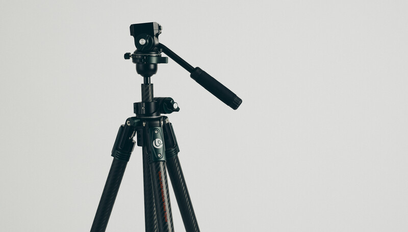 Professional video tripod with fluid head and extended pan handle against a neutral background.