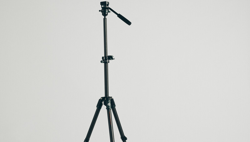 Black tripod with fluid head and pan arm against neutral gray background.
