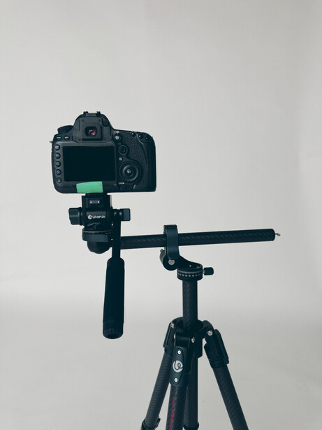 DSLR camera mounted on a tripod with articulating arm and ball head against white background.