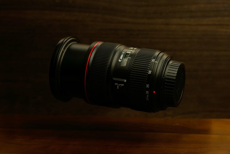 Telephoto zoom lens with red focus ring mounted on wooden surface against dark background.