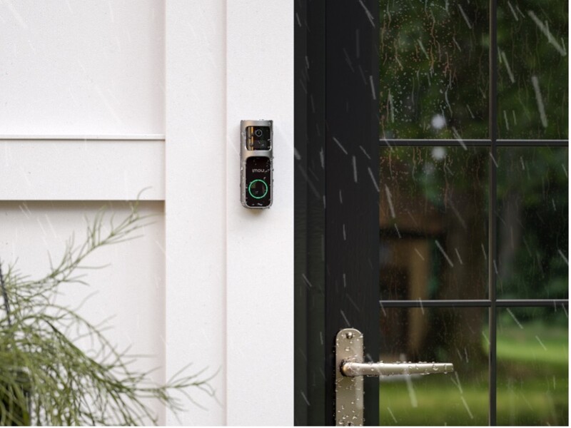 Modern smart doorbell mounted on white exterior wall next to black-framed glass door.