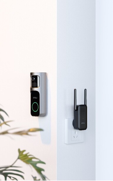 Smart home security devices mounted on a white wall beside decorative plant stems.