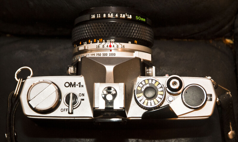 Top-down view of an OM-1n SLR camera with 50mm lens mounted on dark fabric.