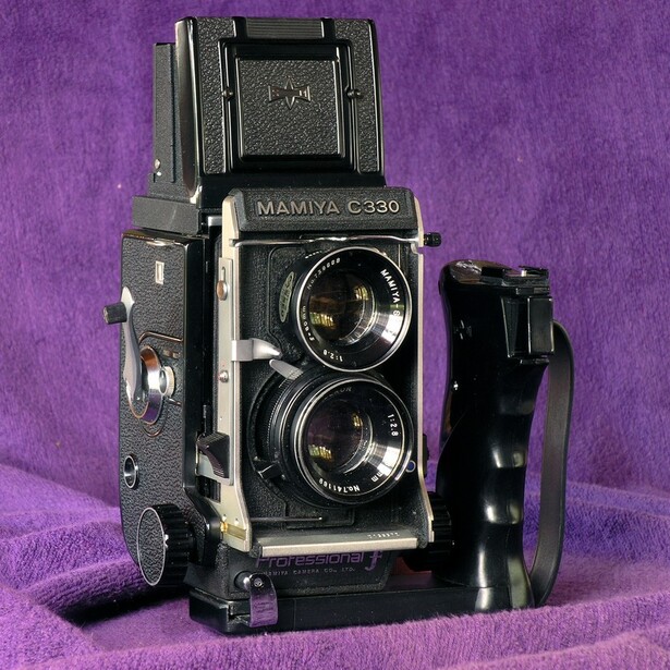 Mamiya C330 twin-lens reflex camera with waist-level viewfinder and strap on purple background.