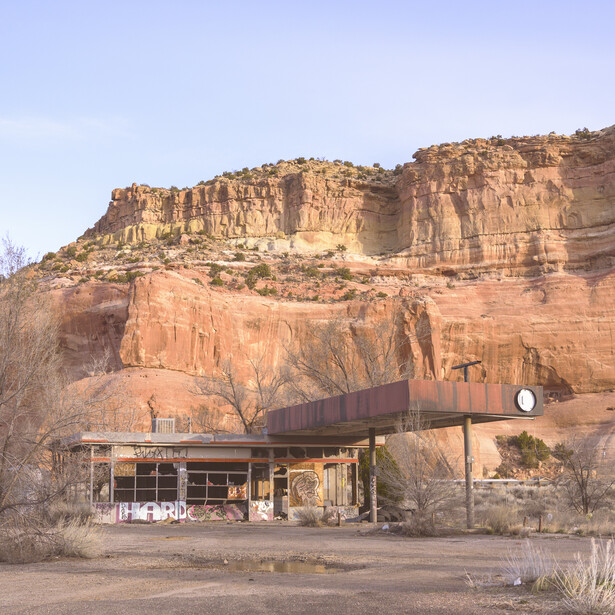 Desert landscape with massive red rock formations towering above a small structure with corrugated metal siding.