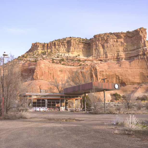 Adobe-colored sandstone cliff face with horizontal columnar jointing rising above a modernist building structure.