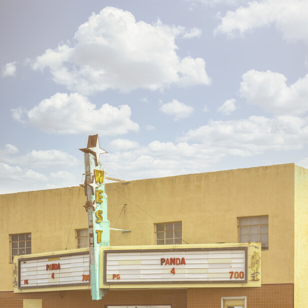 Vintage roadside theater with yellow facade and retro vertical sign against blue sky with white clouds.
