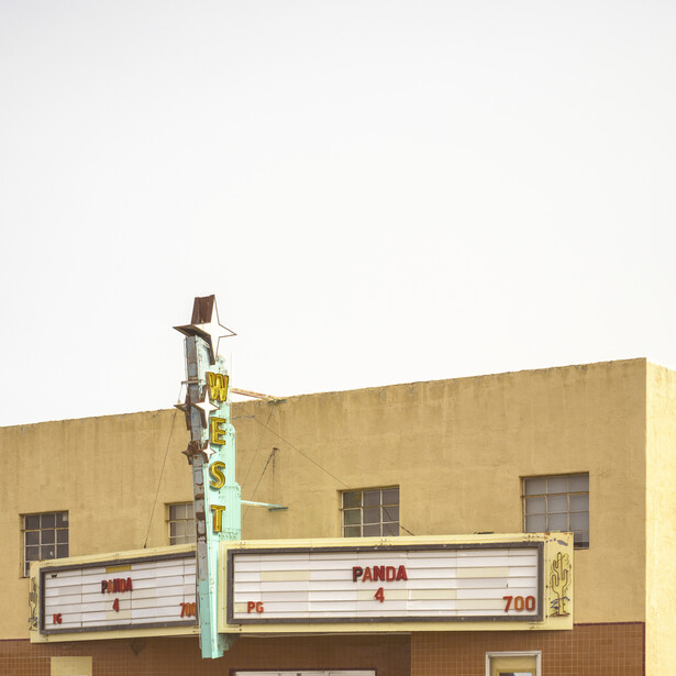 Vintage neon sign mounted on tan-colored building facade with horizontal striped storefront.