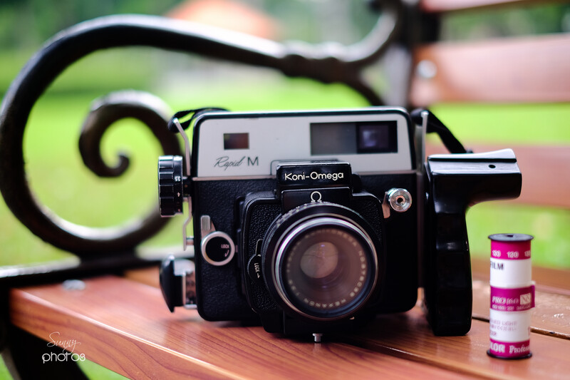 Koni-Omega rangefinder camera with film rolls on wooden surface outdoors.