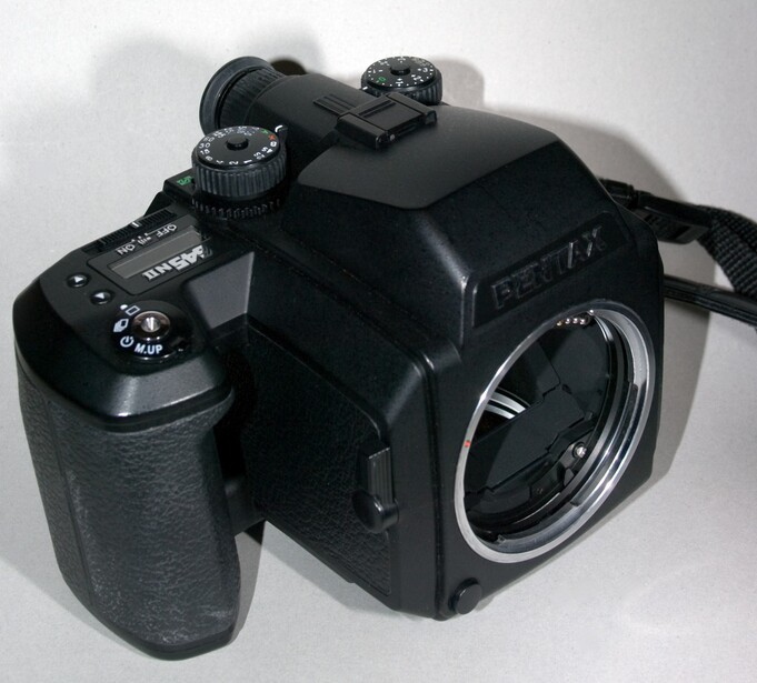 Medium format camera with square film back and hand grip against white background.