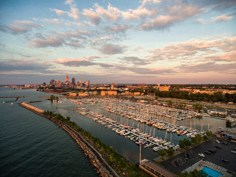 Aerial view of a marina filled with sailboats alongside a waterfront city skyline at sunset.