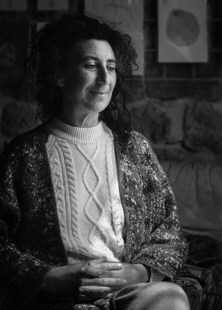 Woman in cable-knit sweater and patterned cardigan gazes downward in black and white portrait.