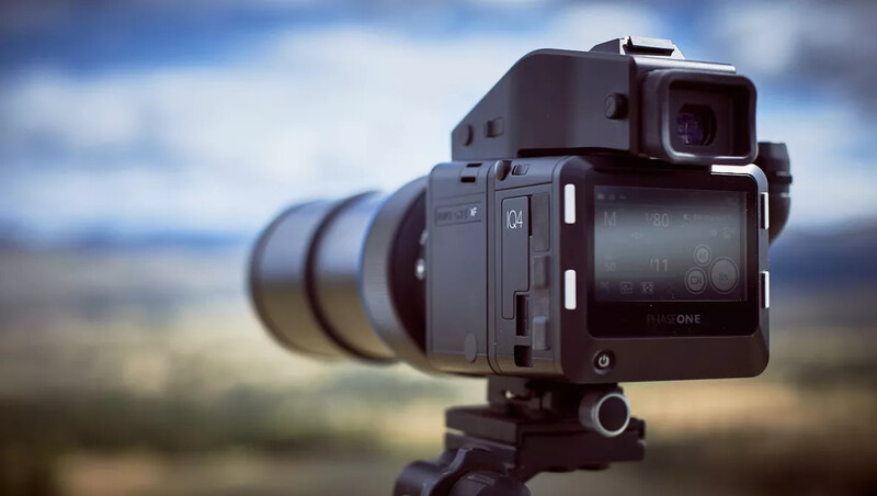 Professional digital camera mounted on tripod with telephoto lens, positioned against blurred landscape background.