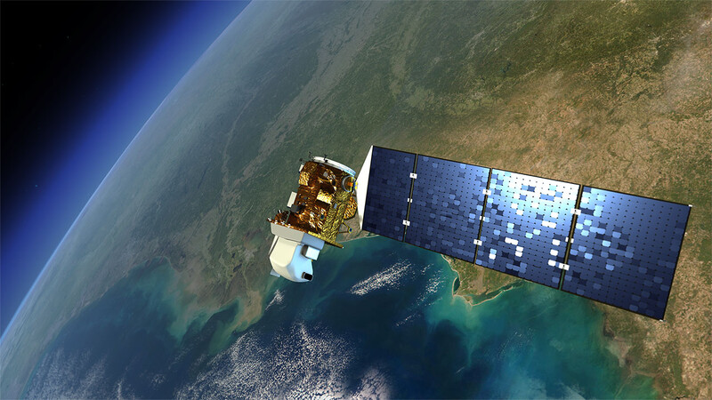 Satellite orbiting Earth with extended solar panels above a coastal region with clouds and ocean.