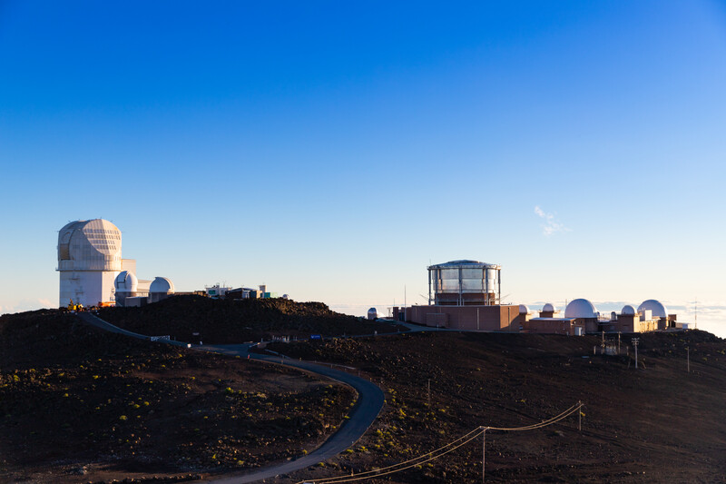 Observatory domes and structures on a volcanic landscape at sunset with clear blue sky.