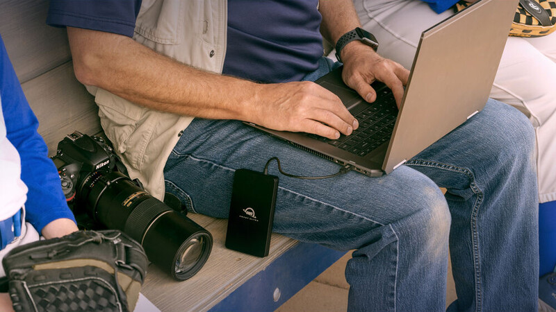 Photographer working on laptop while reviewing digital camera equipment on desk.