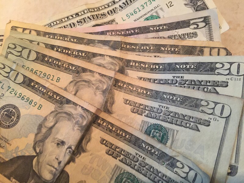 Fanned arrangement of US twenty-dollar bills displaying portrait and serial numbers in natural overhead lighting.