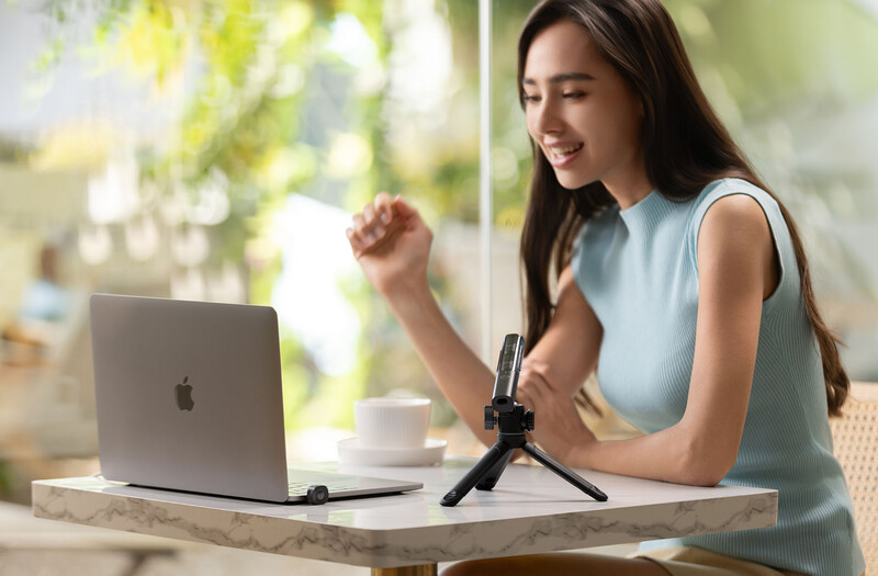 Woman speaking into a microphone mounted on a tripod while seated at a desk with a laptop.